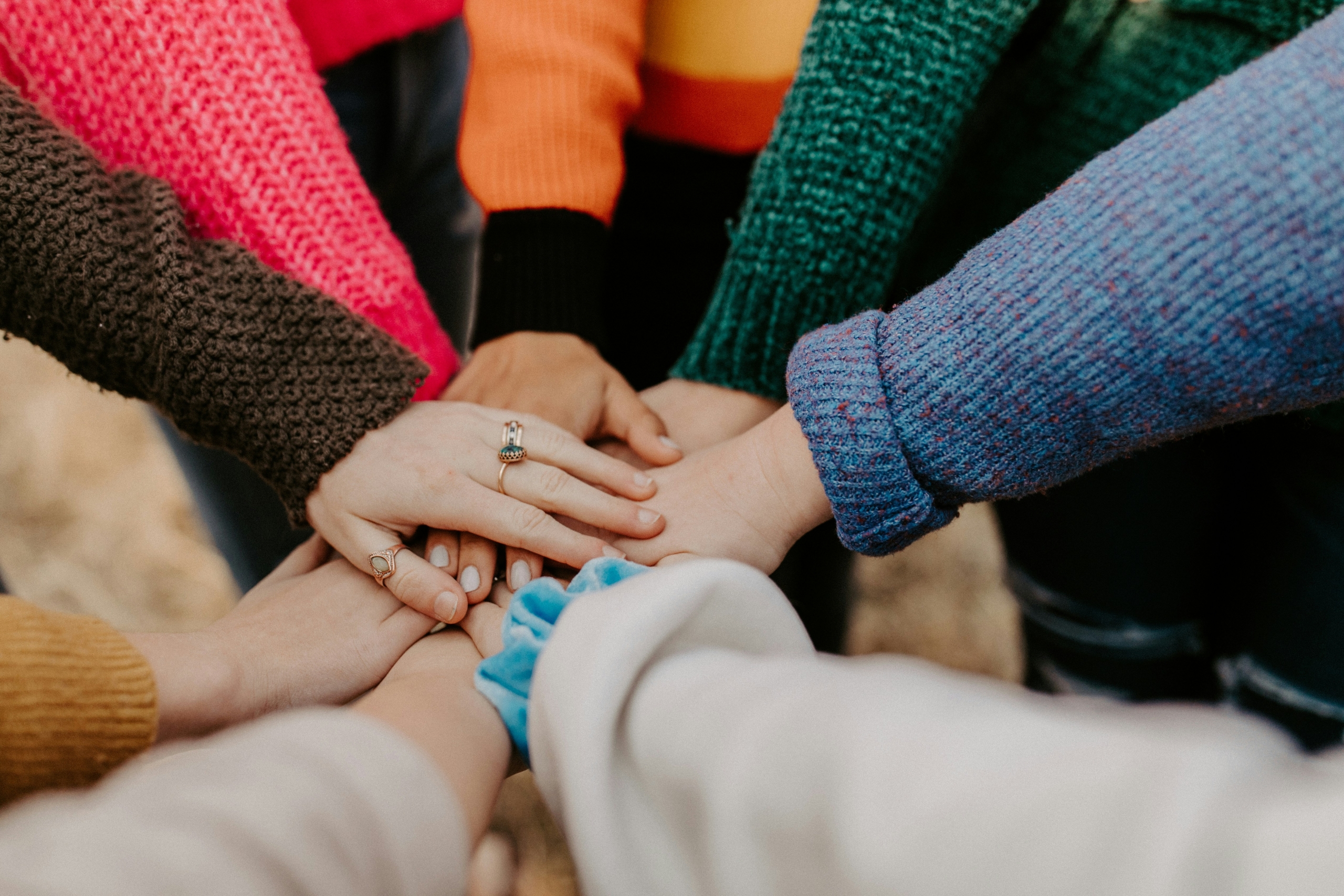 Diverse hands of various skin tones join together in a circle, symbolizing unity and collaboration in a nonprofit organization. The hands, viewed from above, represent people from different backgrounds coming together for a common purpose, illustrating the inclusive nature of nonprofit work and community engagement.